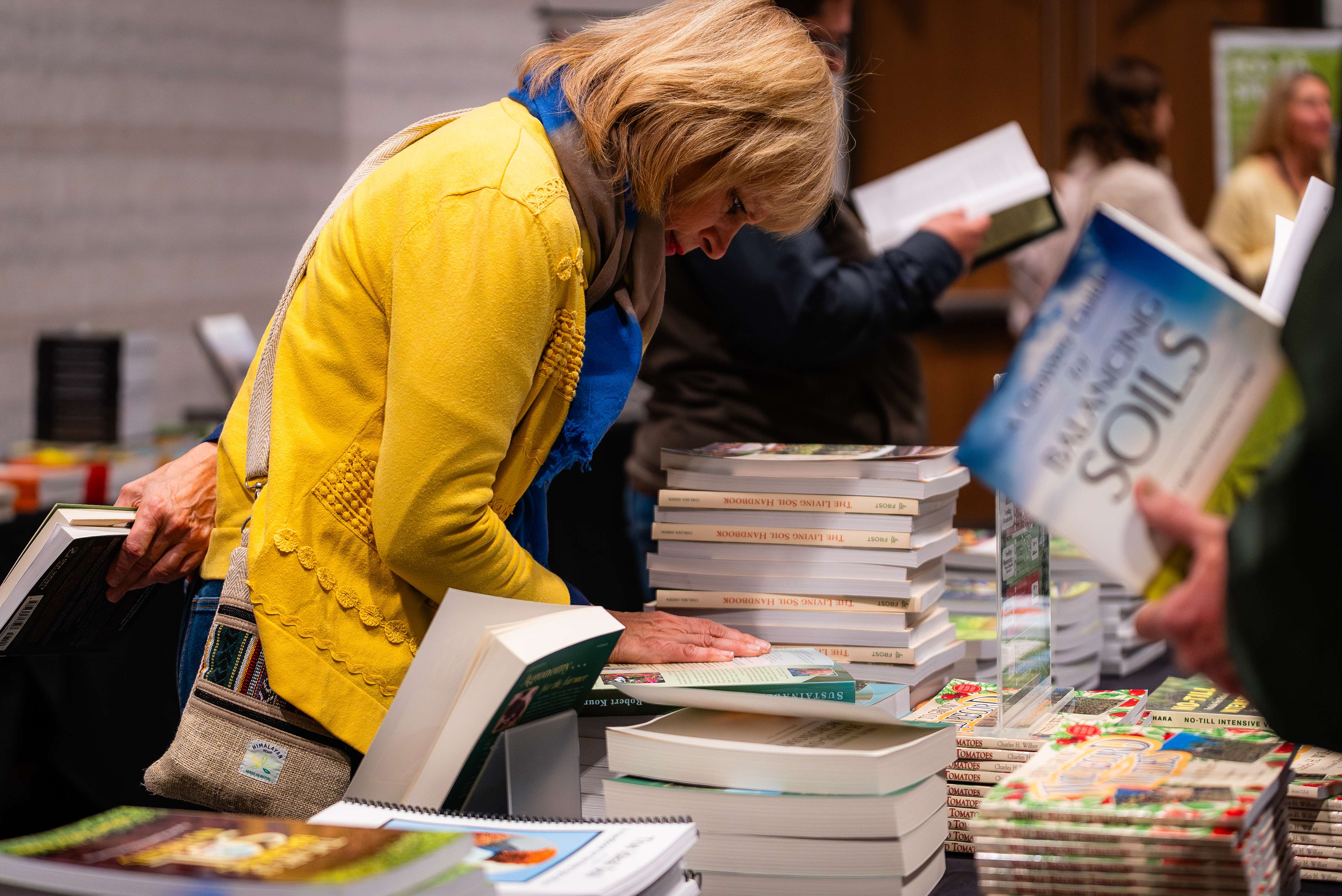 Attendee browsing a table of ecological and regenerative farming books at the on-site bookstore during the Eco-Ag Conference