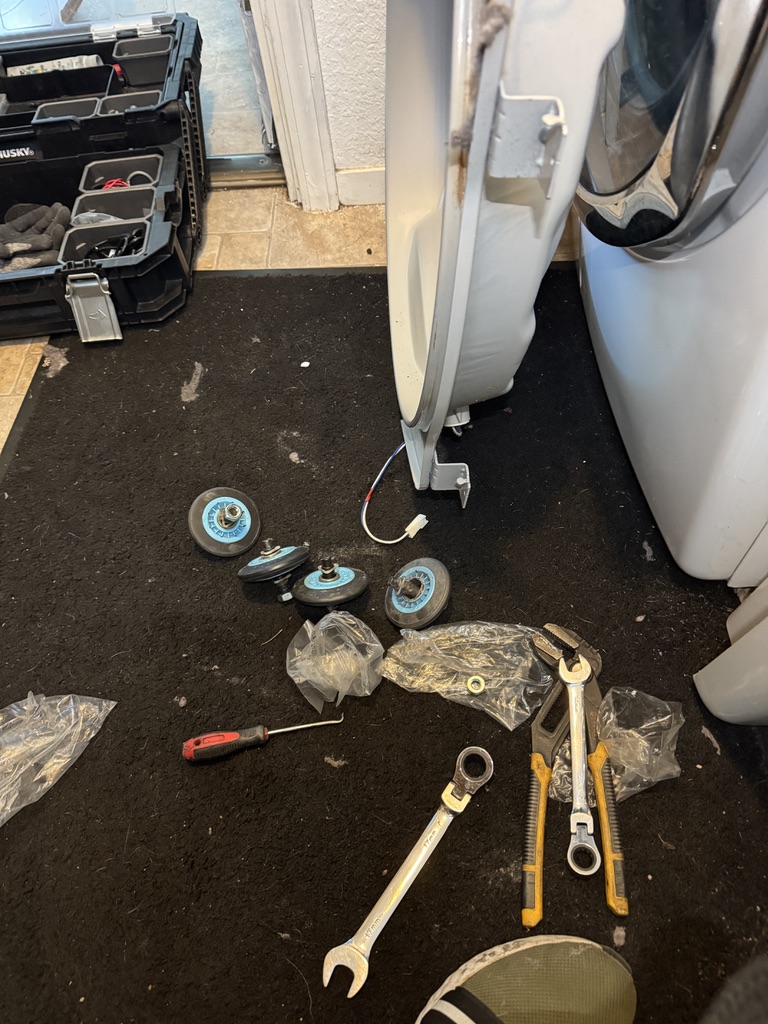 Four removed Samsung dryer drum support rollers beside the disassembled appliance