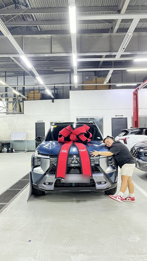 Bhryx hugging a brand-new blue SUV with a big red ribbon at the dealership