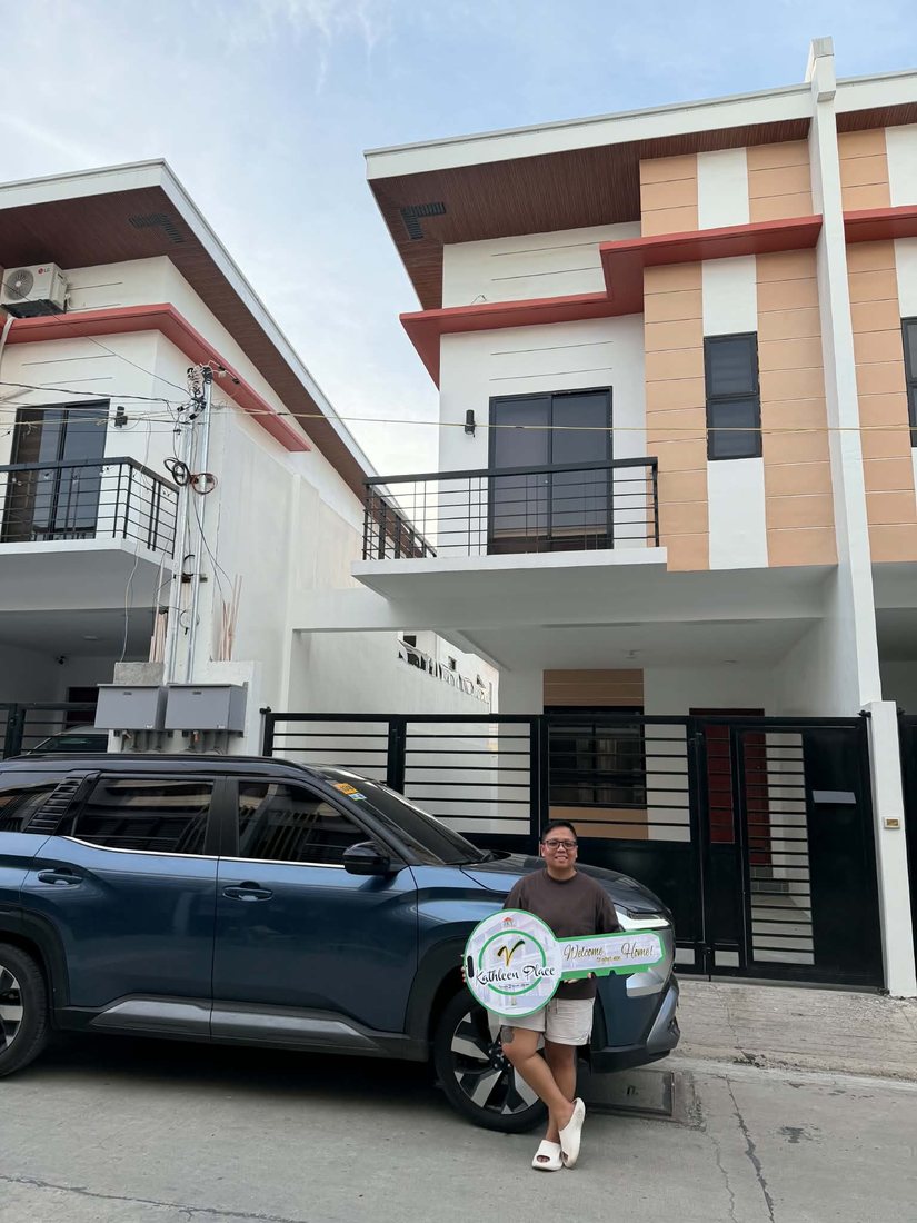 Bhryx holding a welcome-home key sign in front of a new two-storey house, with the SUV parked outside