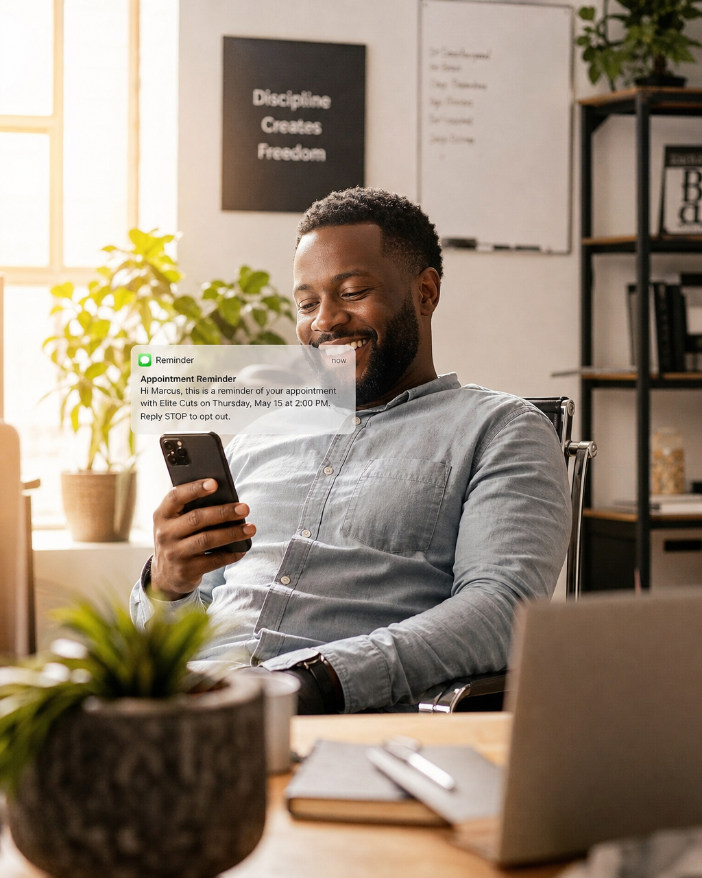 Black man small business owner smiling with relief at an automated appointment reminder on his phone in a bright sunny office Black man small business owner smiling with relief at an automated appointment reminder on his phone in a bright sunny office