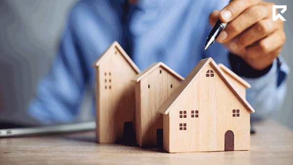 Real estate professional planning property transactions using miniature house models on a desk. Concept image representing property valuations, real estate sales, housing market analysis, property investment decisions, and estate agent services for buyers and sellers.