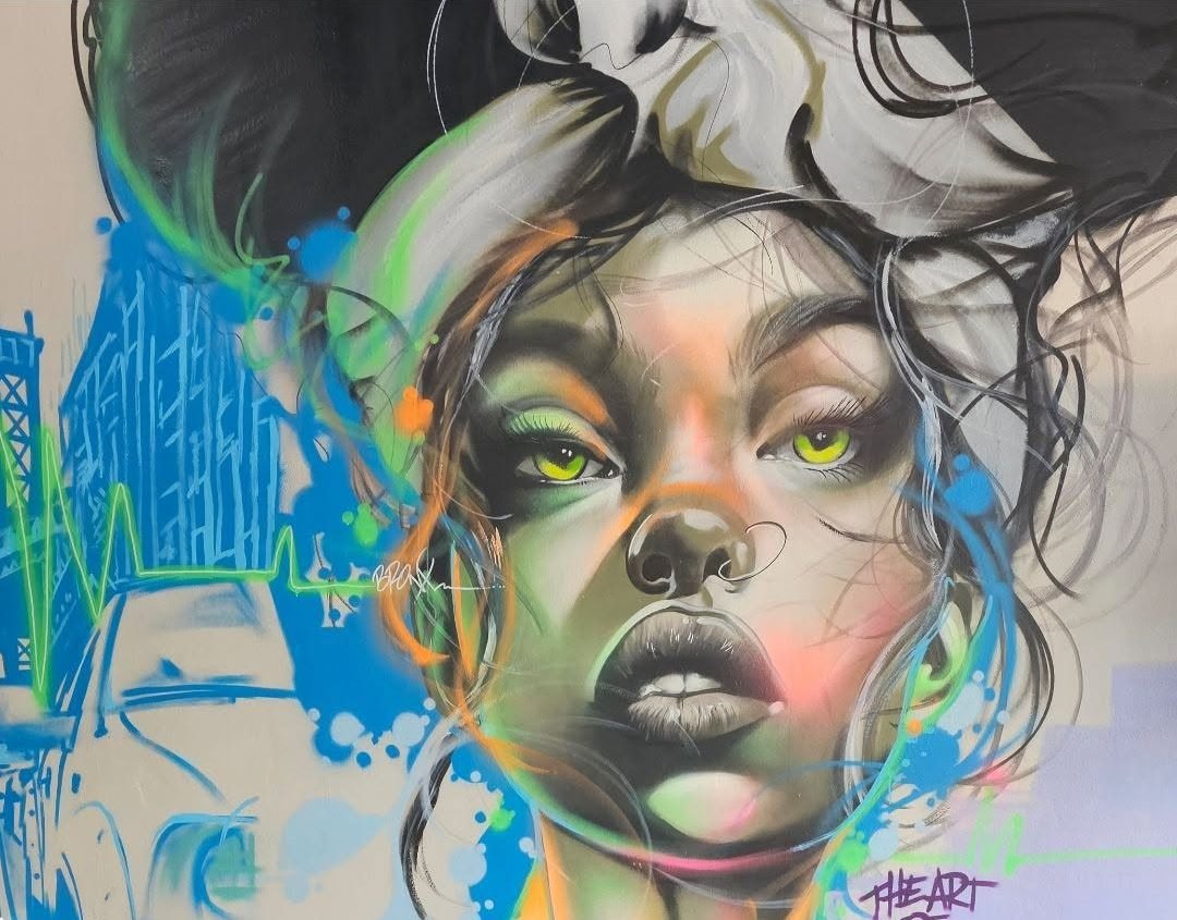 Spray-painted mural on the shop wall: a woman's face in black and grey with green eyes, wrapped in strokes of blue, orange and neon green