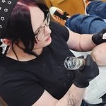 Emma in glasses and black gloves, tattooing