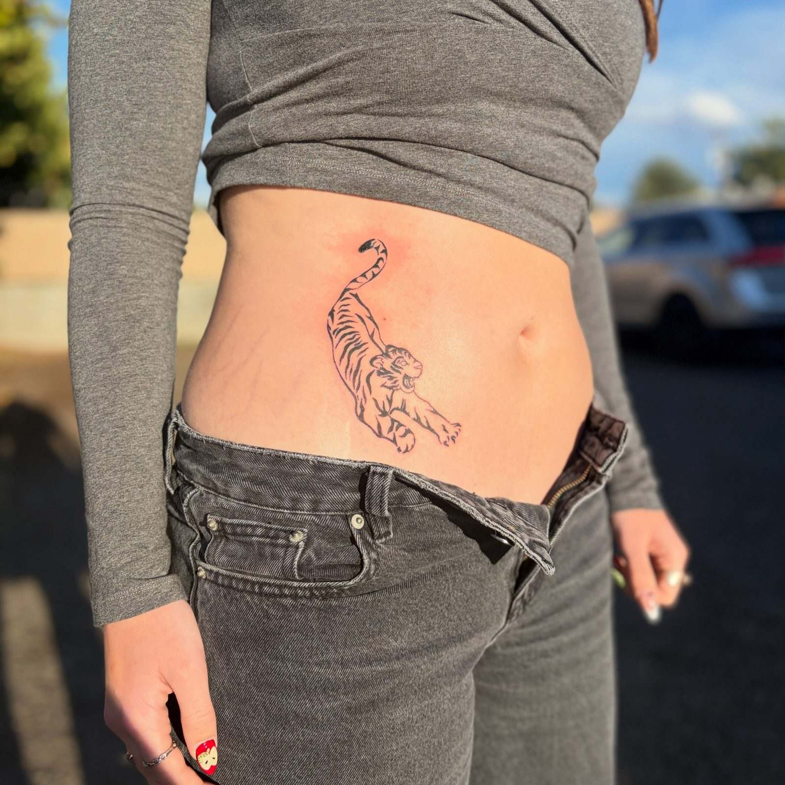 Black and grey tiger climbing up the side of the stomach, by Peyton
