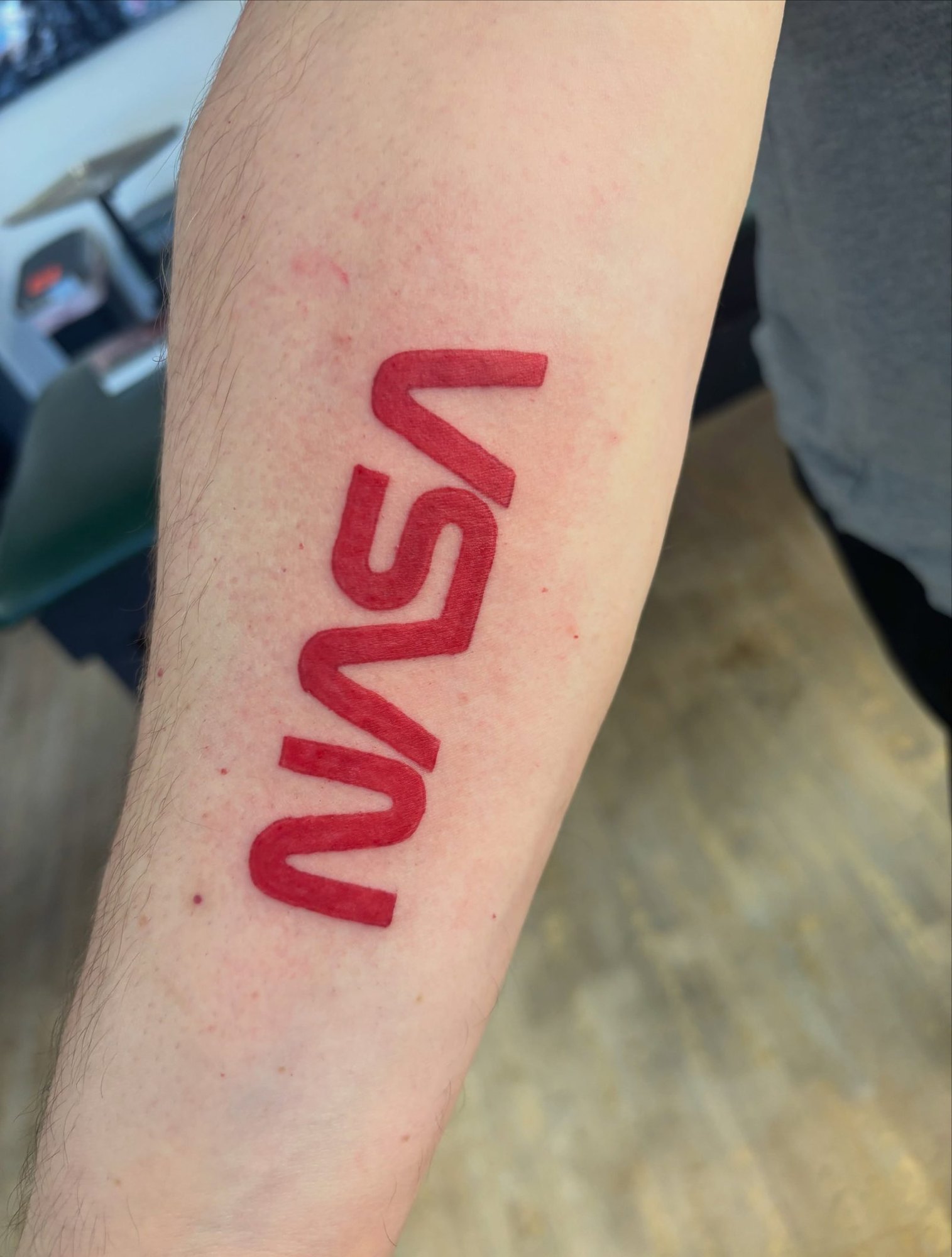The red NASA worm logo running down the inner forearm, by Carmelo