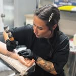 Iyla Rose in black gloves, leaning in to tattoo an arm