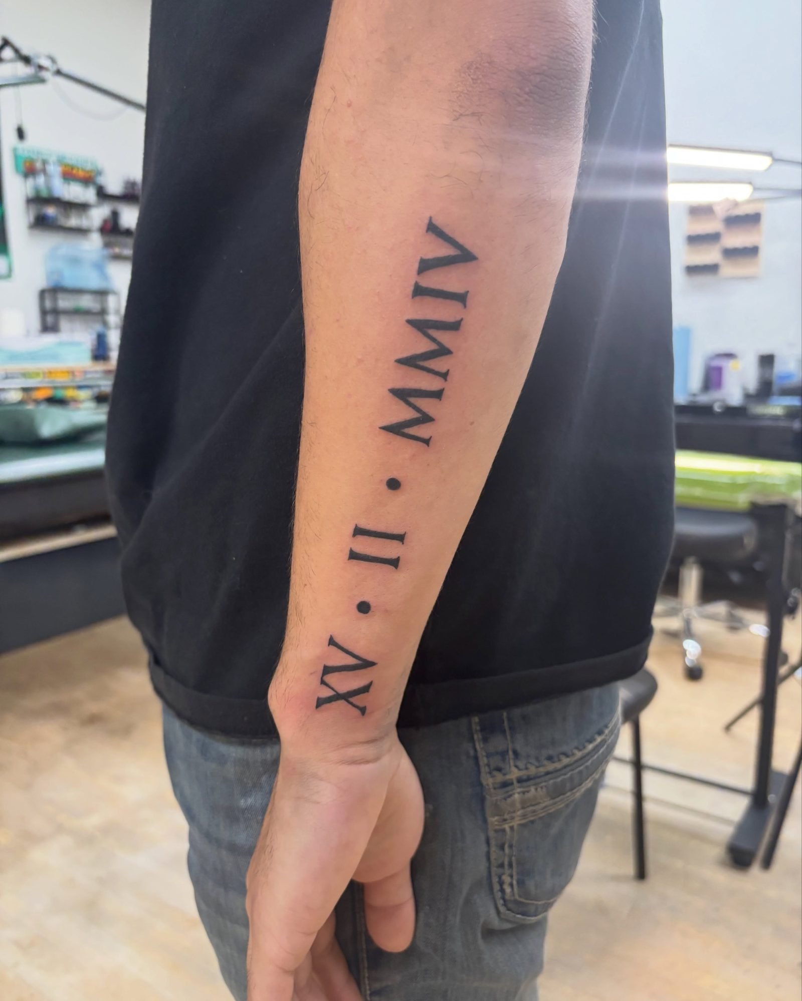 Roman numeral date XV · II · MMIV in serif lettering down the forearm, by Carmelo
