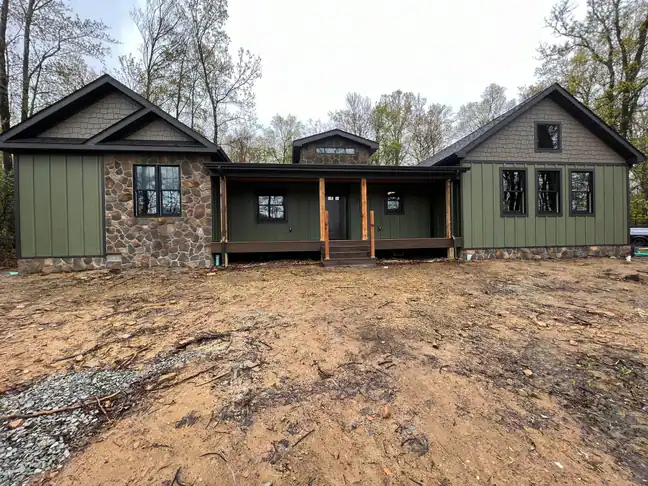 Finished green board-and-batten cottage exterior with stone veneer and a covered front porch
