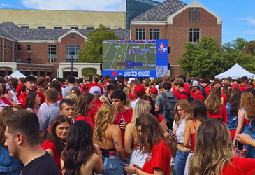 Game-day crowd in red gathered around an LED screen at a college tailgate