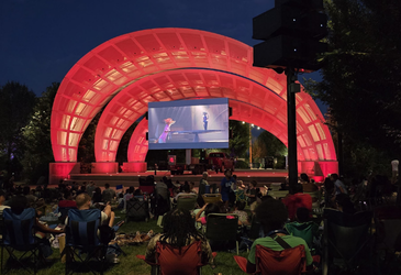 Large LED screen at an outdoor concert under a lit band shell at night