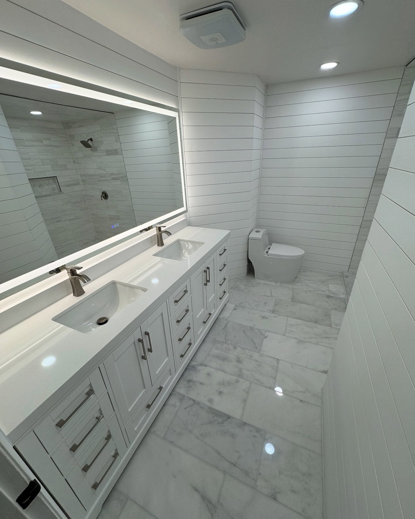 Double vanity with lit mirror and shiplap wall by Demo Gods
