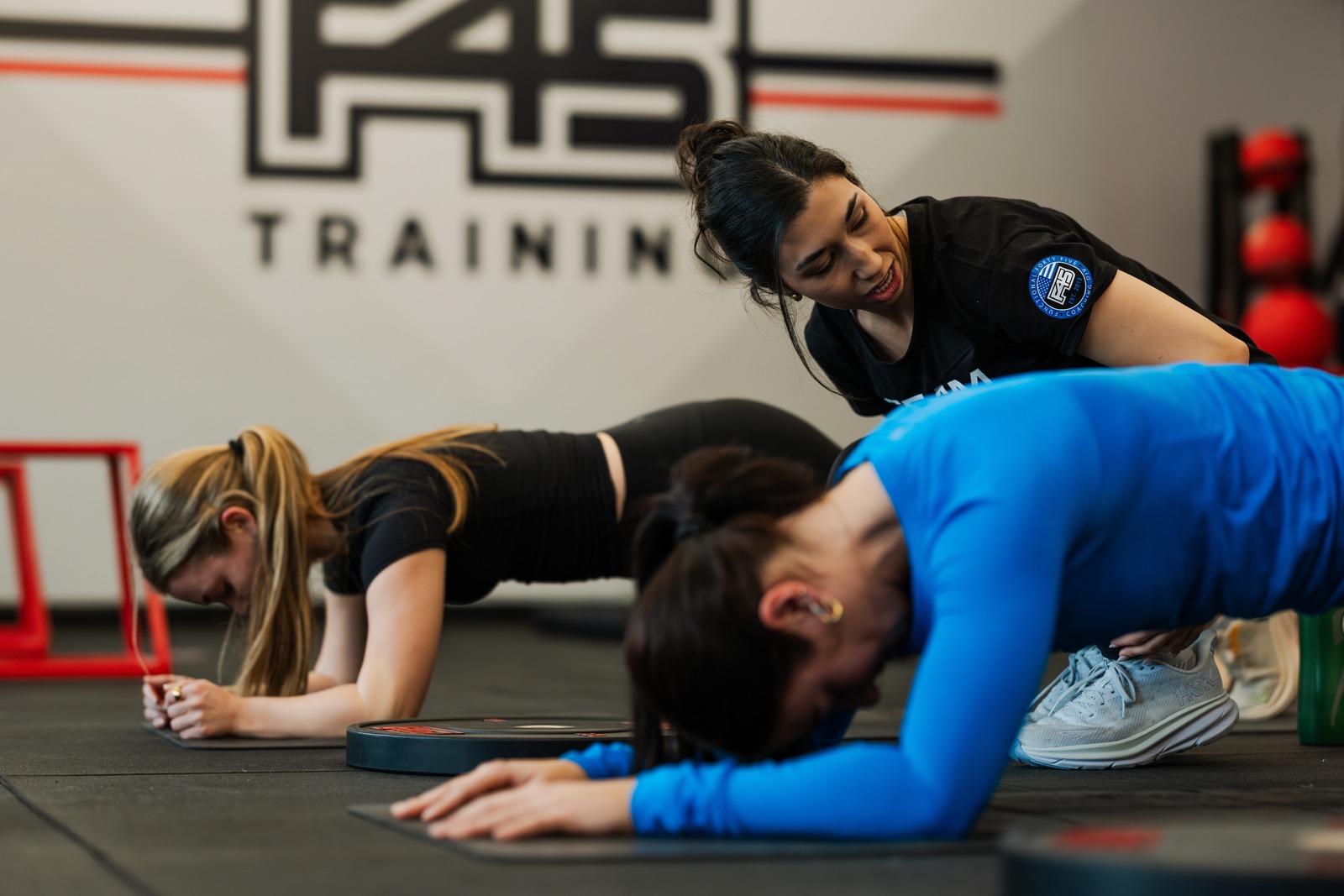 F45 coach guiding two members through core work in front of the F45 Training wall