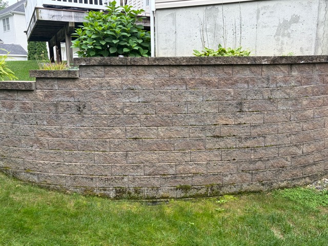 Retaining wall with dirt, algae, and organic buildup before cleaning by Thin Red Line Pressure Washing in Clifton Park, NY.