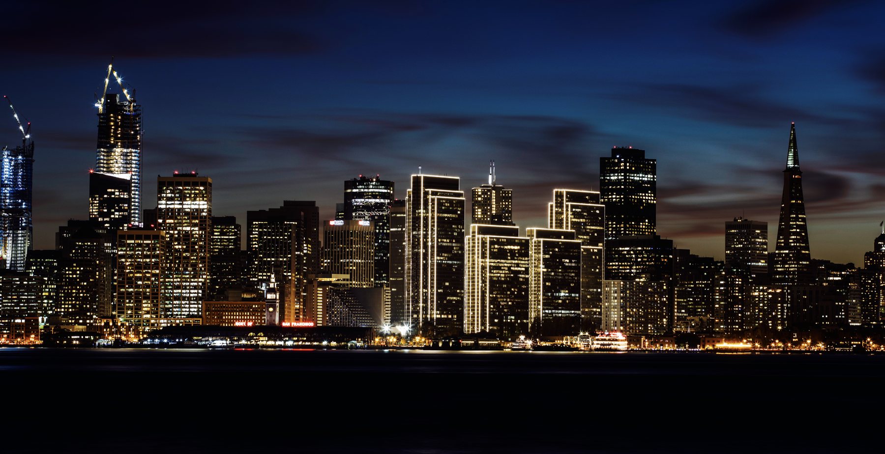San Francisco skyline at dusk seen across the bay from Treasure Island, with the Transamerica Pyramid and Embarcadero towers lit