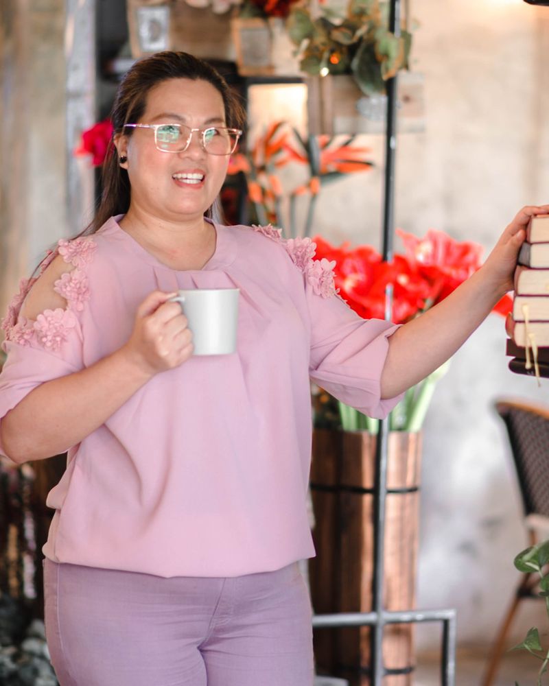 Jackie Cabrera holding a coffee mug beside a bookshelf, smiling