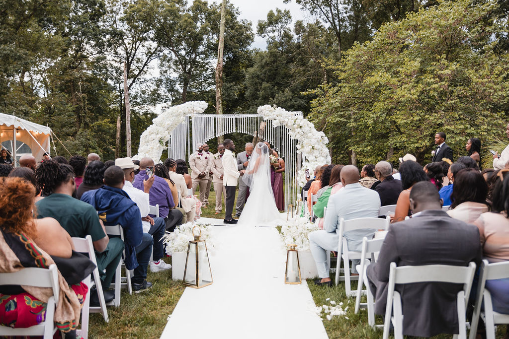 Outdoor wedding ceremony with a white floral arch and gold lanterns by MJ Event Designs