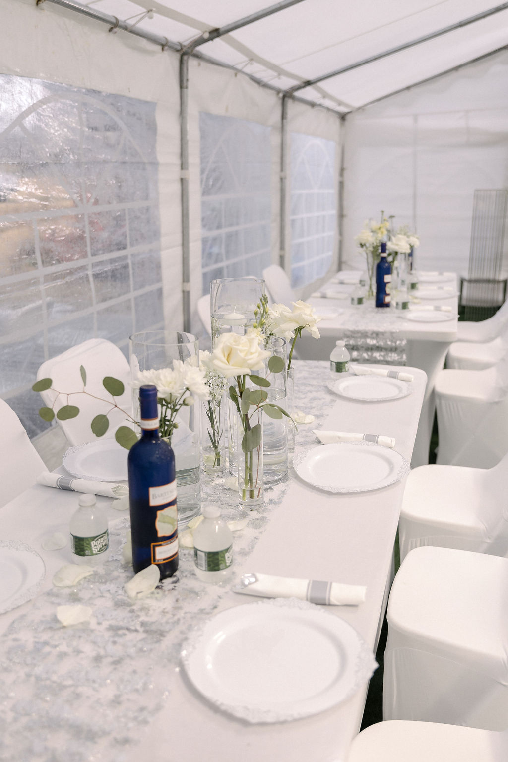 Tented wedding reception with a rectangular banquet table and white chair covers by MJ Event Designs