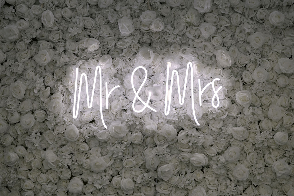 Mr and Mrs neon sign on a white rose flower wall by MJ Event Designs