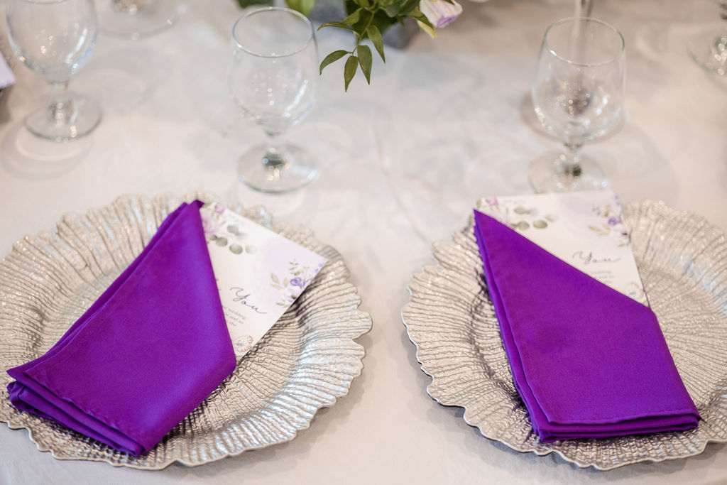 Formal wedding table setting with a purple napkin, silver plate and crystal goblet by MJ Event Designs