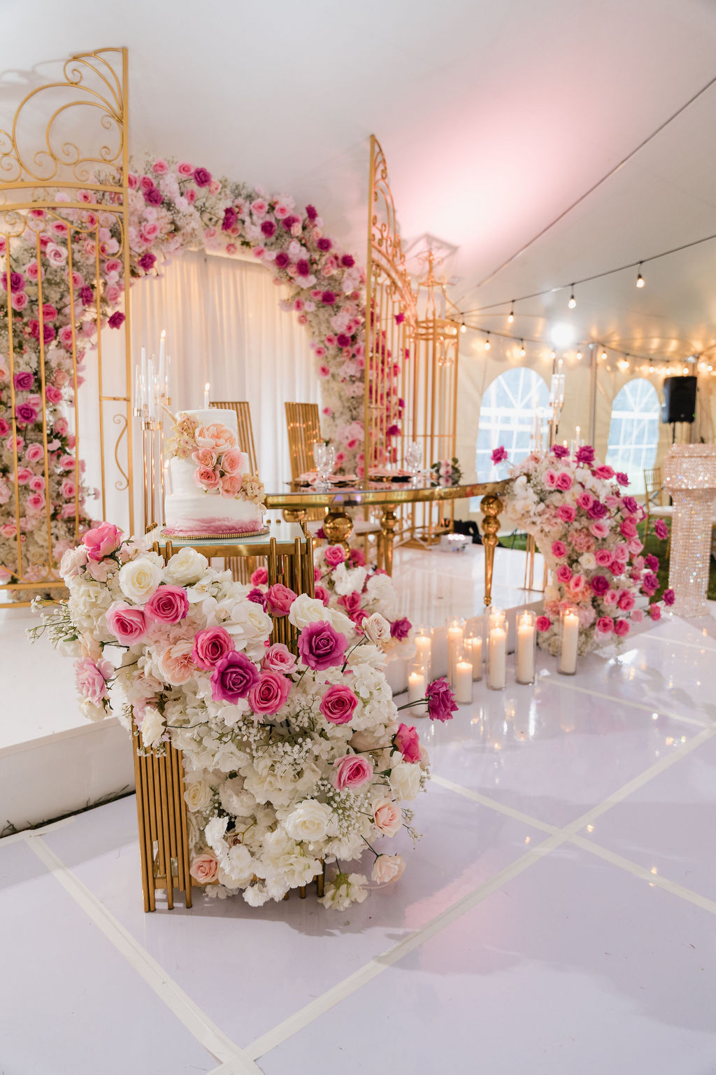 Sweetheart table beneath a gold lattice arch with pink and white roses by MJ Event Designs
