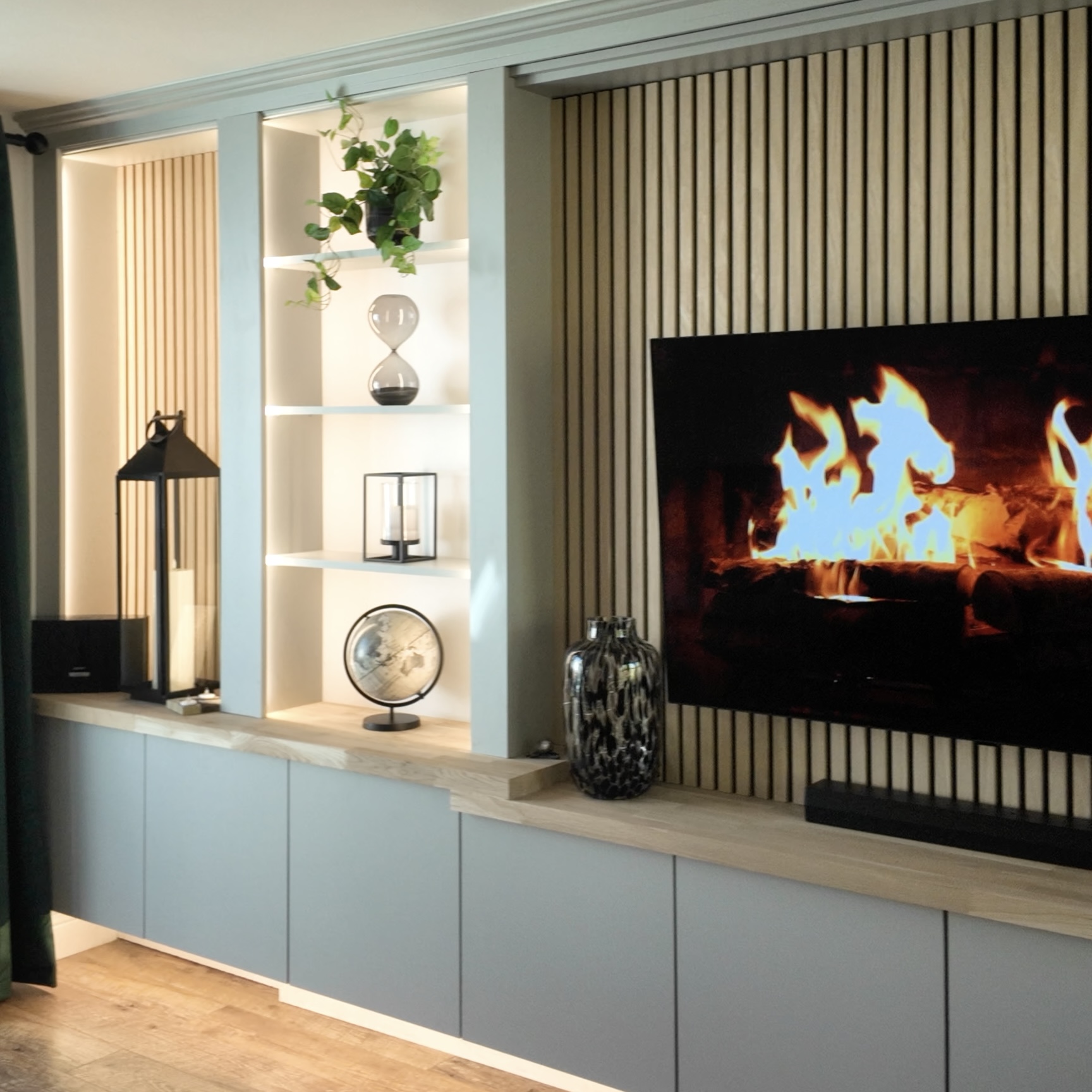 Bespoke slat media wall with fire-effect TV and built-in shelving by The Media Wall Co.