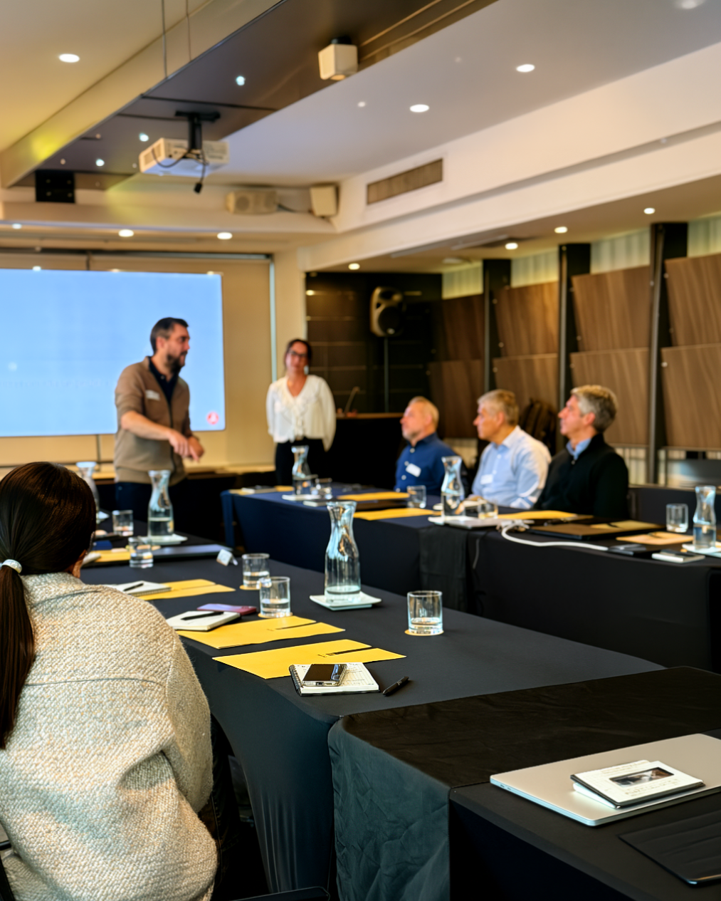 Reunión de equipo con un líder exponiendo ante colaboradores en una mesa de trabajo.