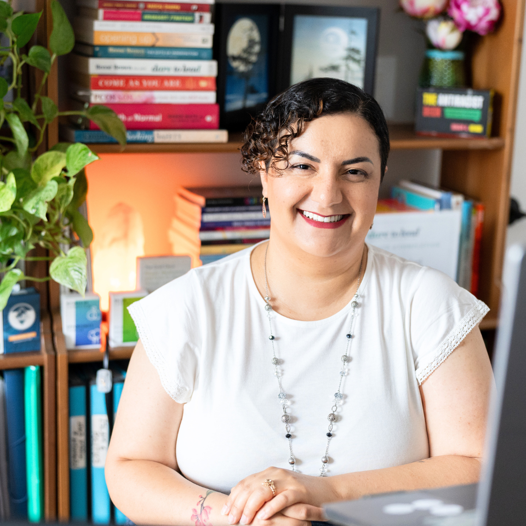 Forouz Salari wearing white t-shirt, smiling, sitting at her desk in her office