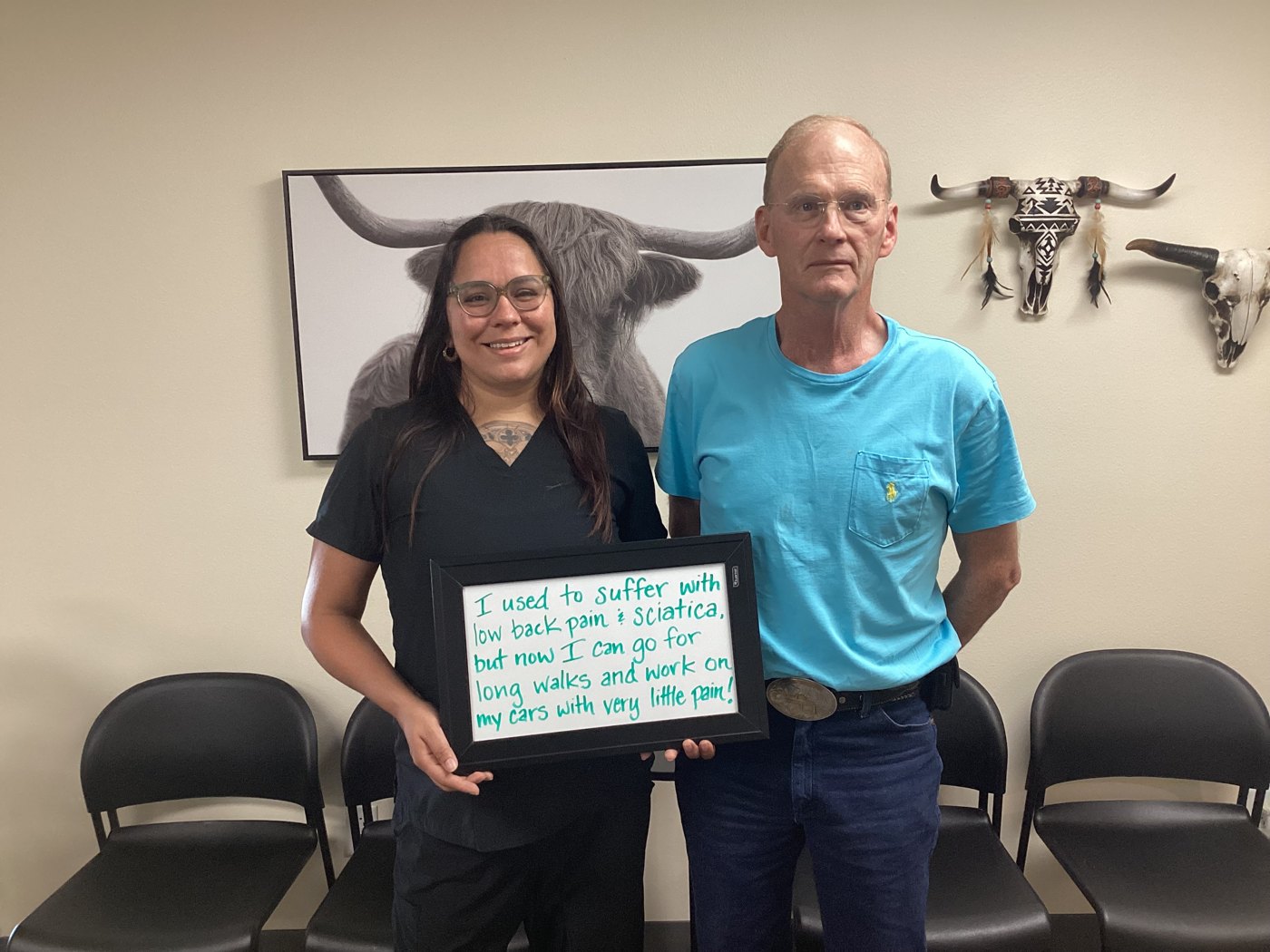 Patient Jess holding a whiteboard about his low back pain and sciatica progress with an Althoff Wellness Clinic team member