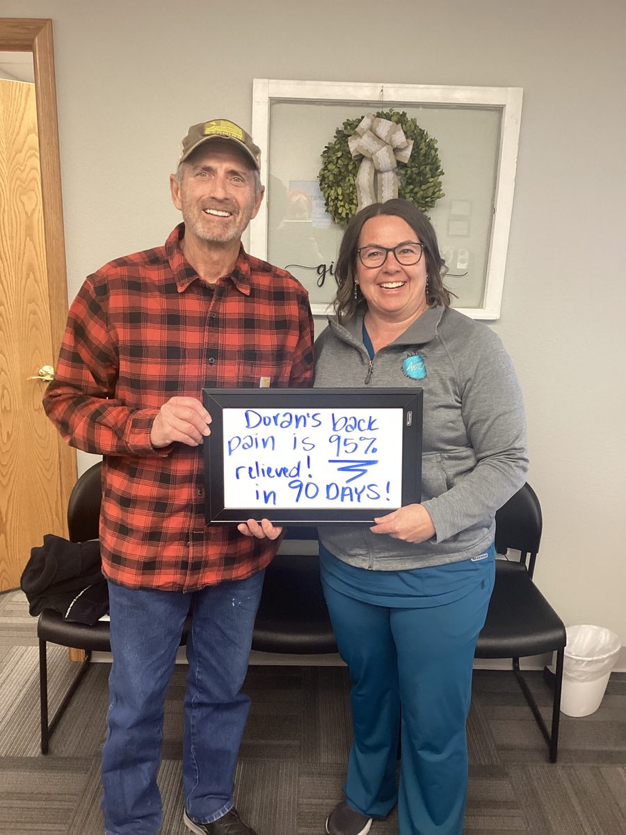 Patient Doran holding a whiteboard about his back pain progress with an Althoff Wellness Clinic team member