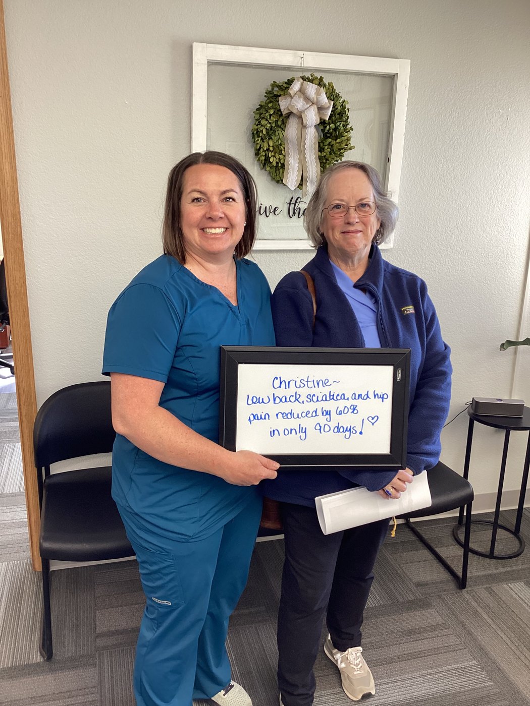 Patient Christine holding a whiteboard about her low back, sciatica, and hip pain progress with an Althoff Wellness Clinic team member