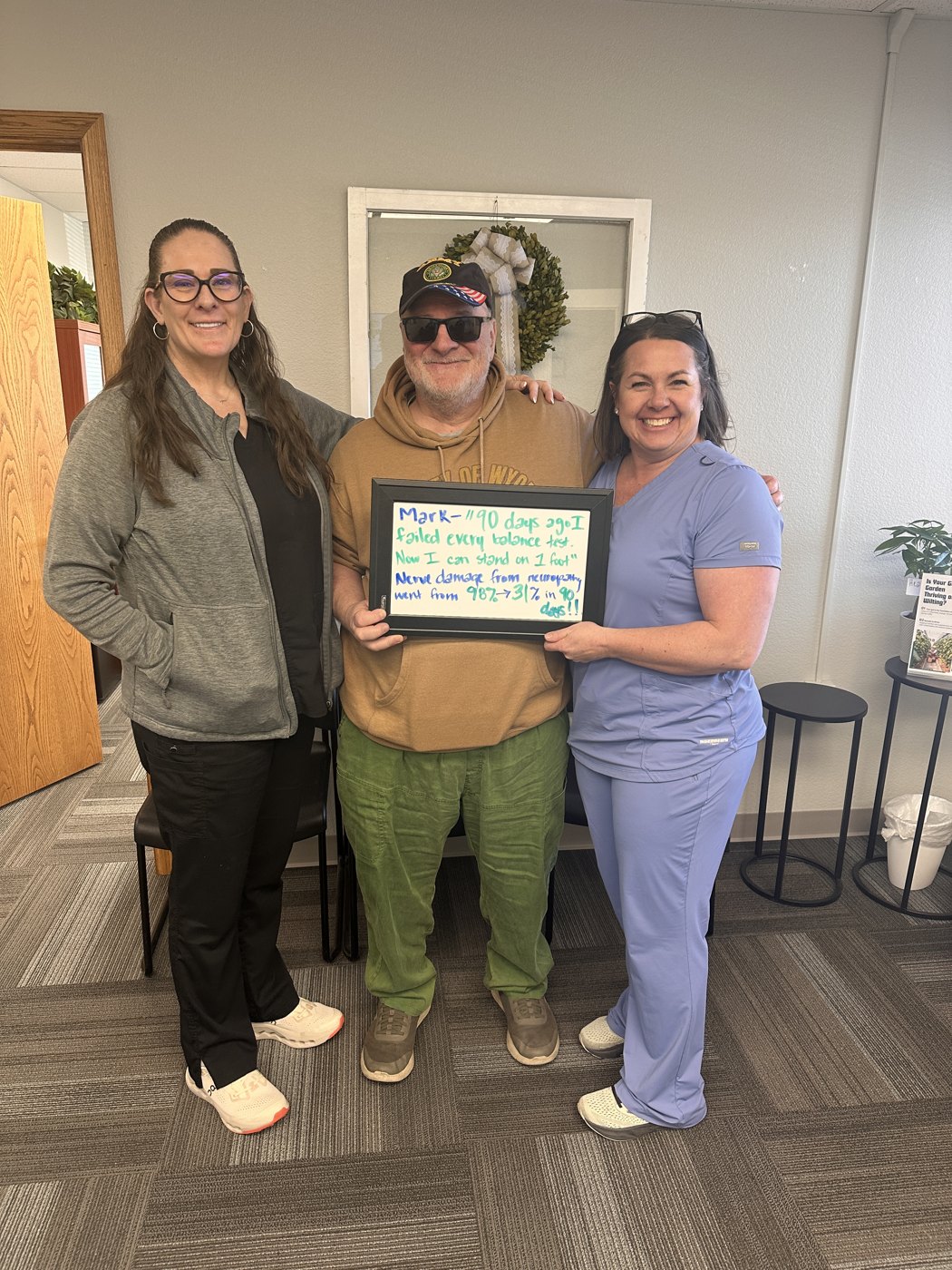 Patient Mark holding a whiteboard about his neuropathy and balance progress with Althoff Wellness Clinic team members in Cheyenne