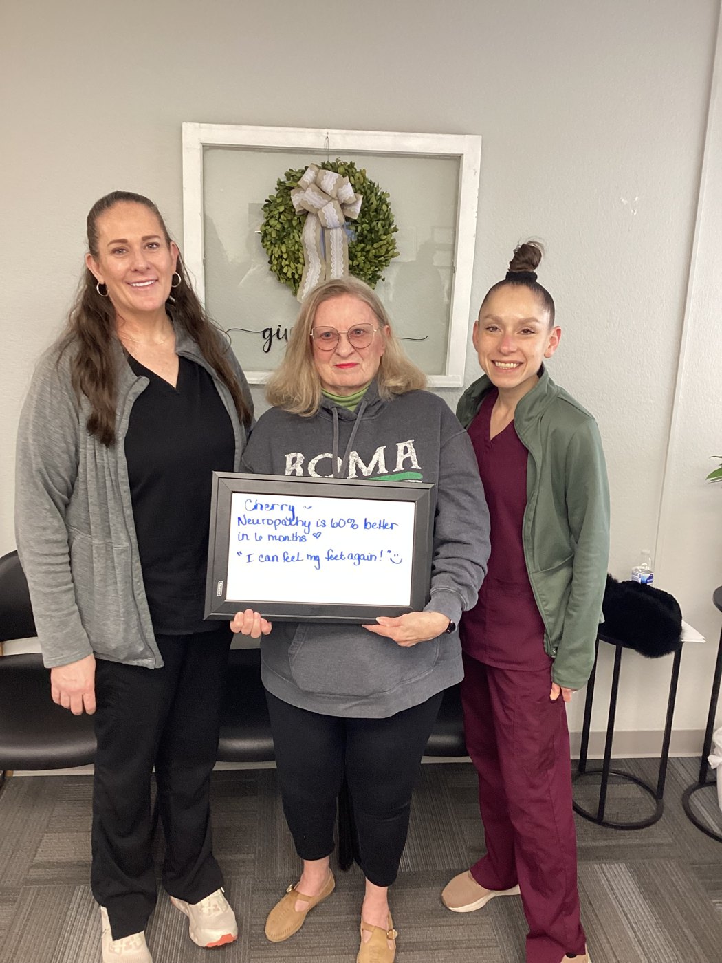 Patient Cherry holding a whiteboard about her neuropathy progress with Althoff Wellness Clinic team members in Cheyenne