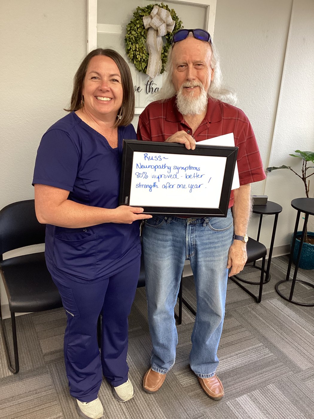 Patient Russ holding a whiteboard about his neuropathy progress with Althoff Wellness Clinic team members in Cheyenne