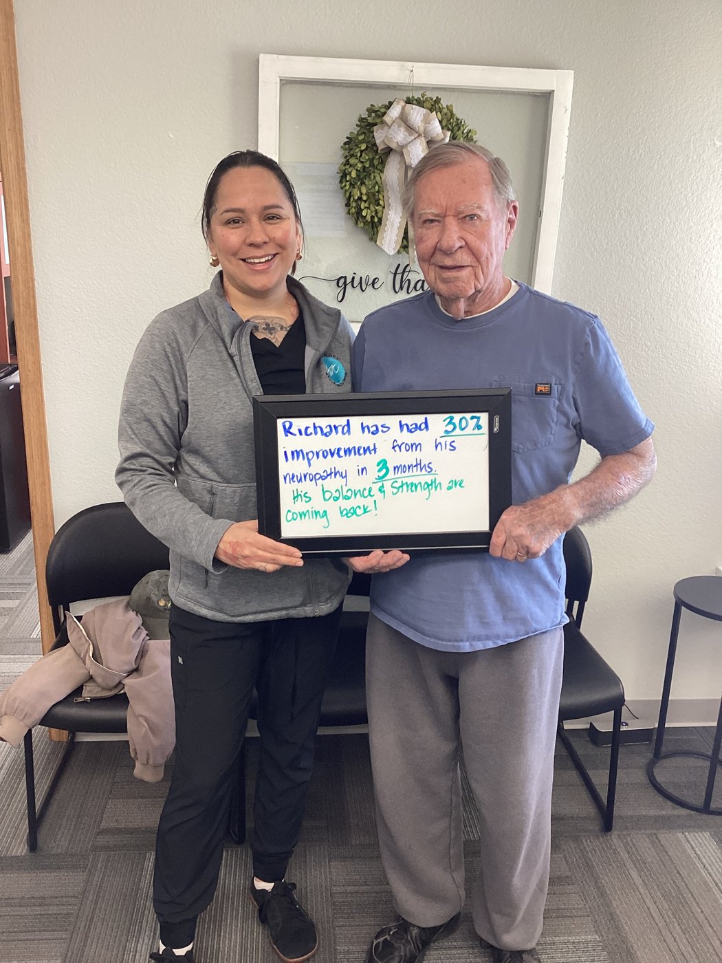 Patient Richard holding a whiteboard about his neuropathy progress with Althoff Wellness Clinic team members in Cheyenne