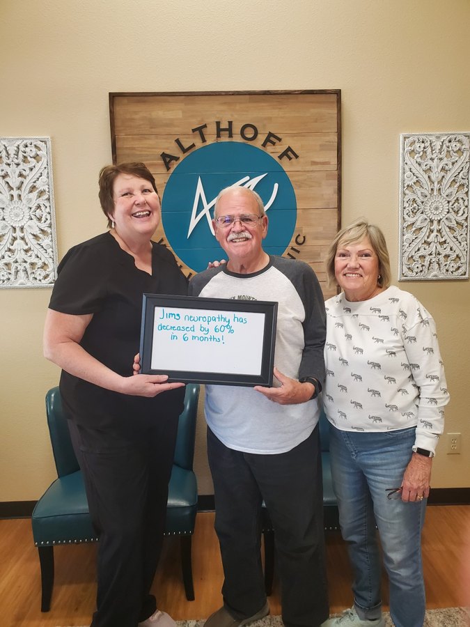 Patient Jim holding a whiteboard about his neuropathy progress with Althoff Wellness Clinic team members
