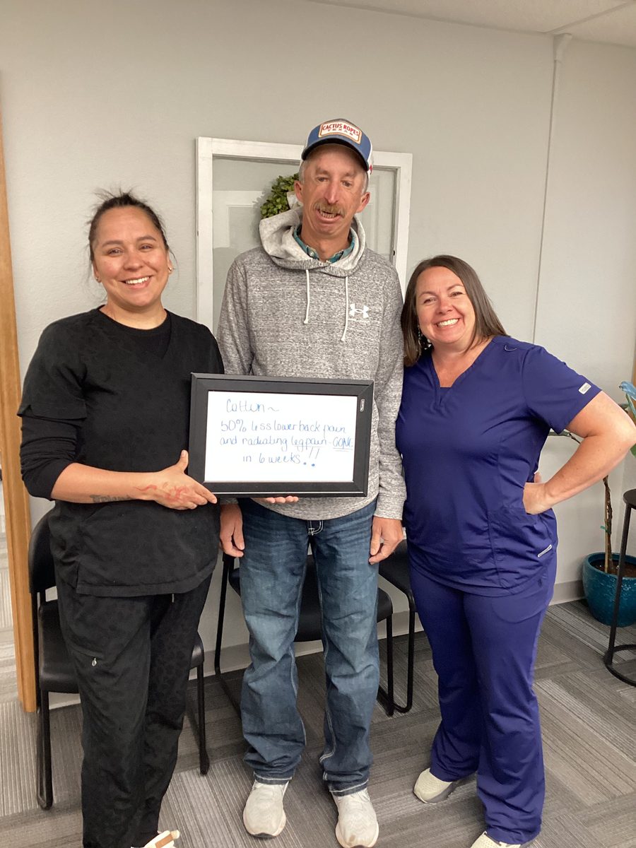 Patient Cotton holding a whiteboard about his lower back and leg pain progress with two Althoff Wellness Clinic team members