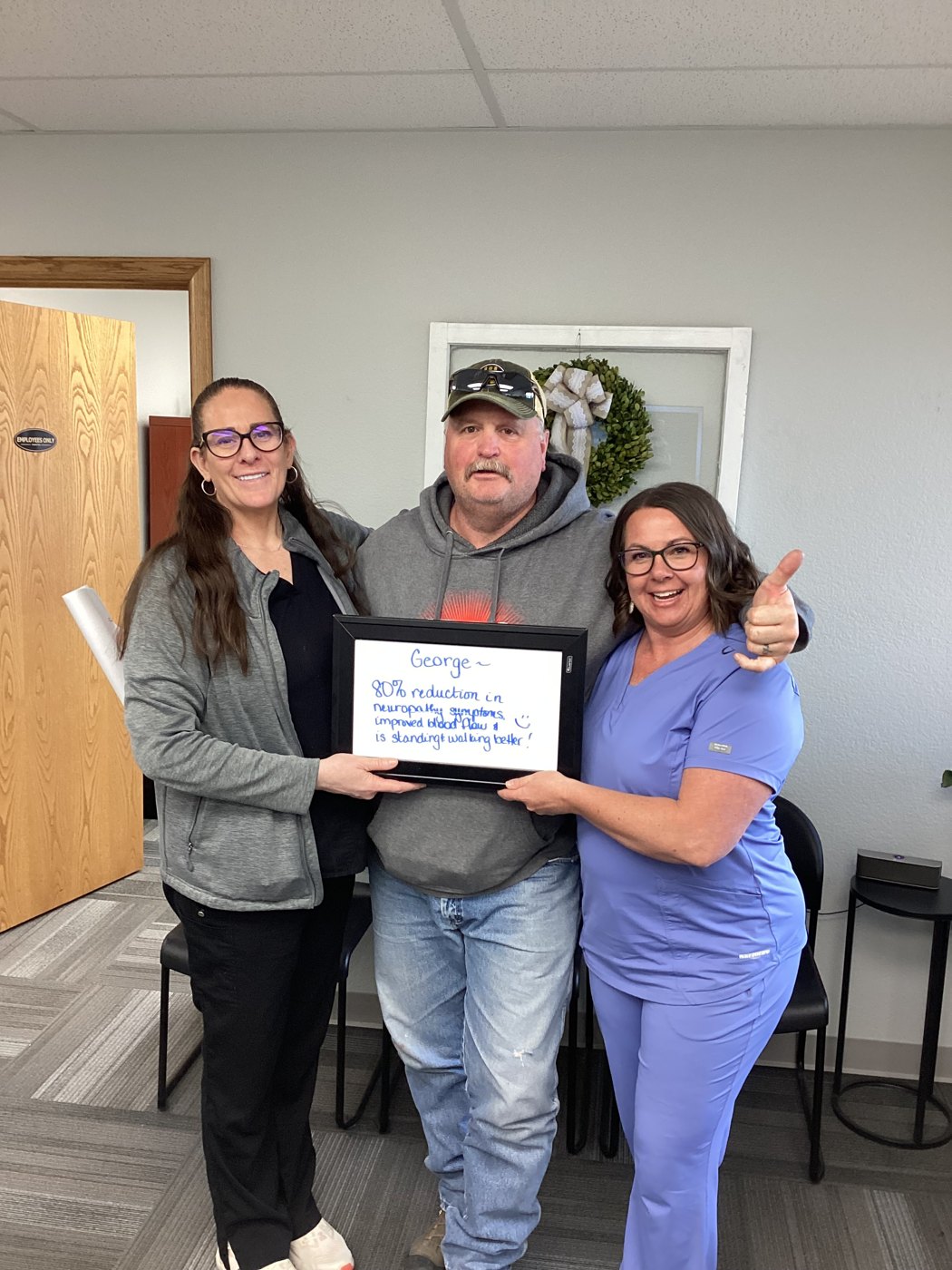 Patient George holding a whiteboard about his neuropathy progress with Althoff Wellness Clinic team members in Cheyenne
