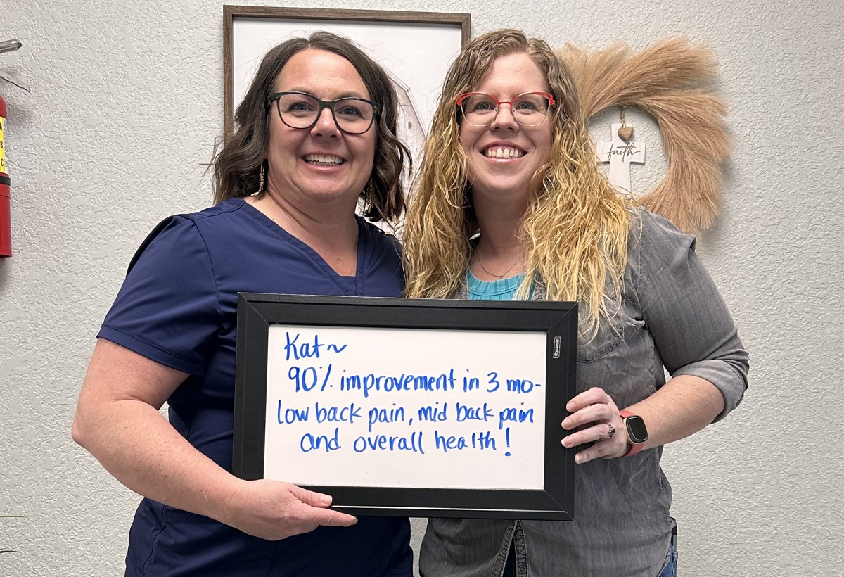 Kat holding a whiteboard about her low and mid back pain progress with an Althoff Wellness Clinic team member in Cheyenne