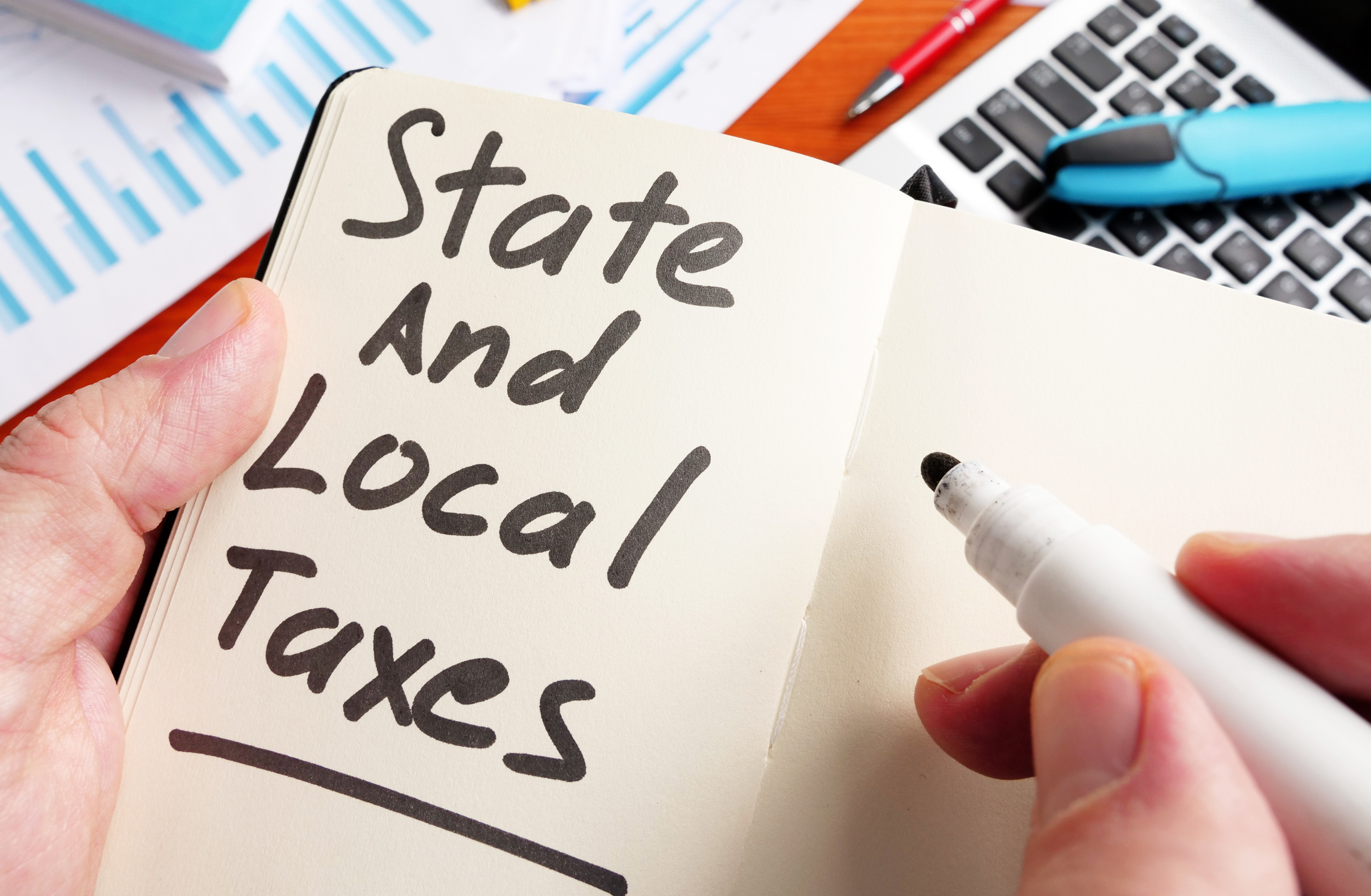 Notebook page reading ‘State and Local Taxes’ beside calculator and financial charts, highlighting law firm SALT tax planning and compliance.
