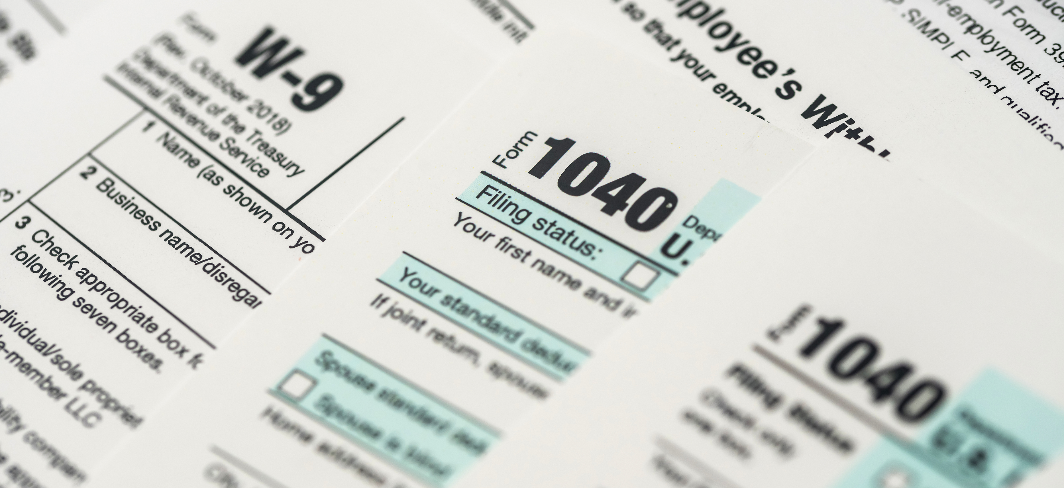 Close-up of IRS tax forms W-9, W-4, and Form 1040, representing law firm payroll, contractor payments, and annual tax filing.