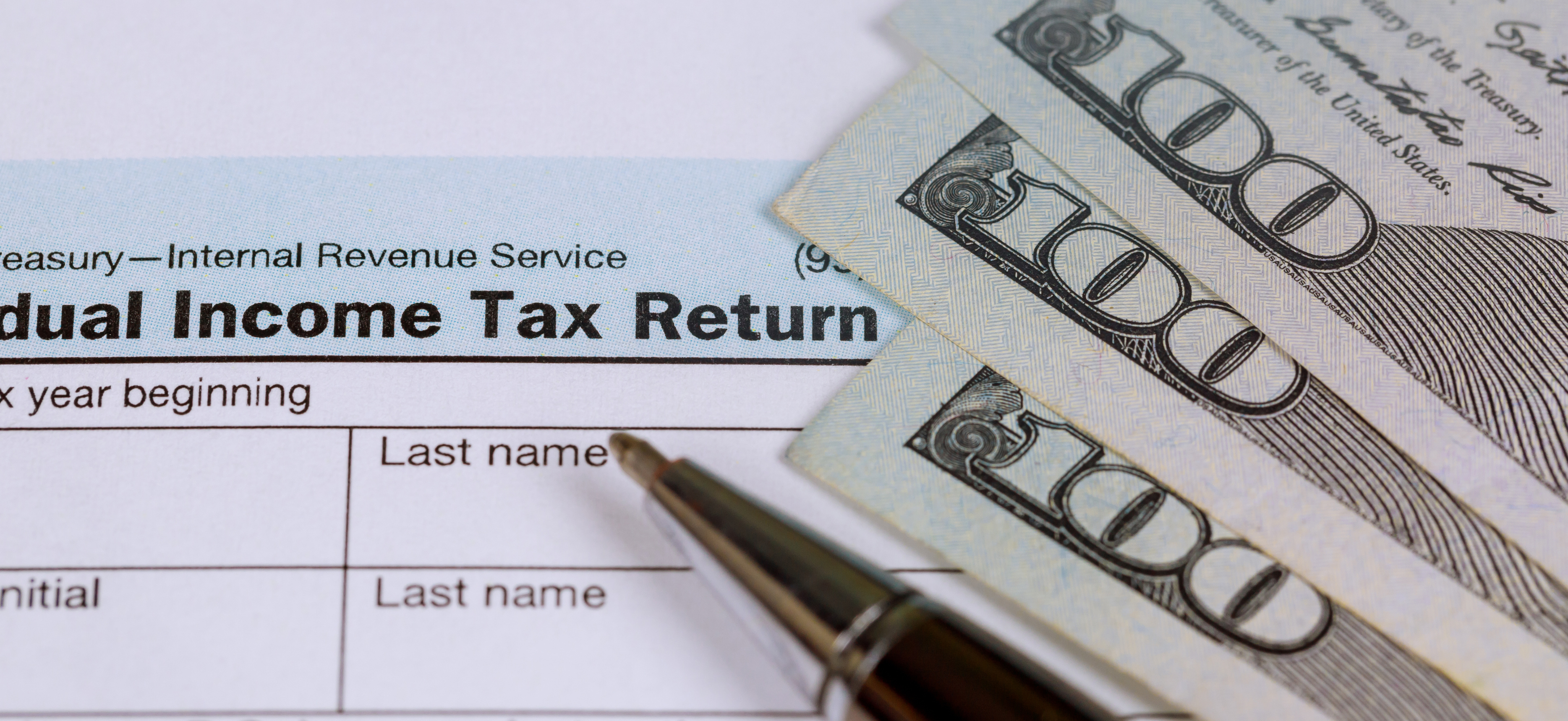 A lawyer's close-up of IRS Tax Return with $100 bills and a pen, illustrating law firm owner tax planning and cash reserves.