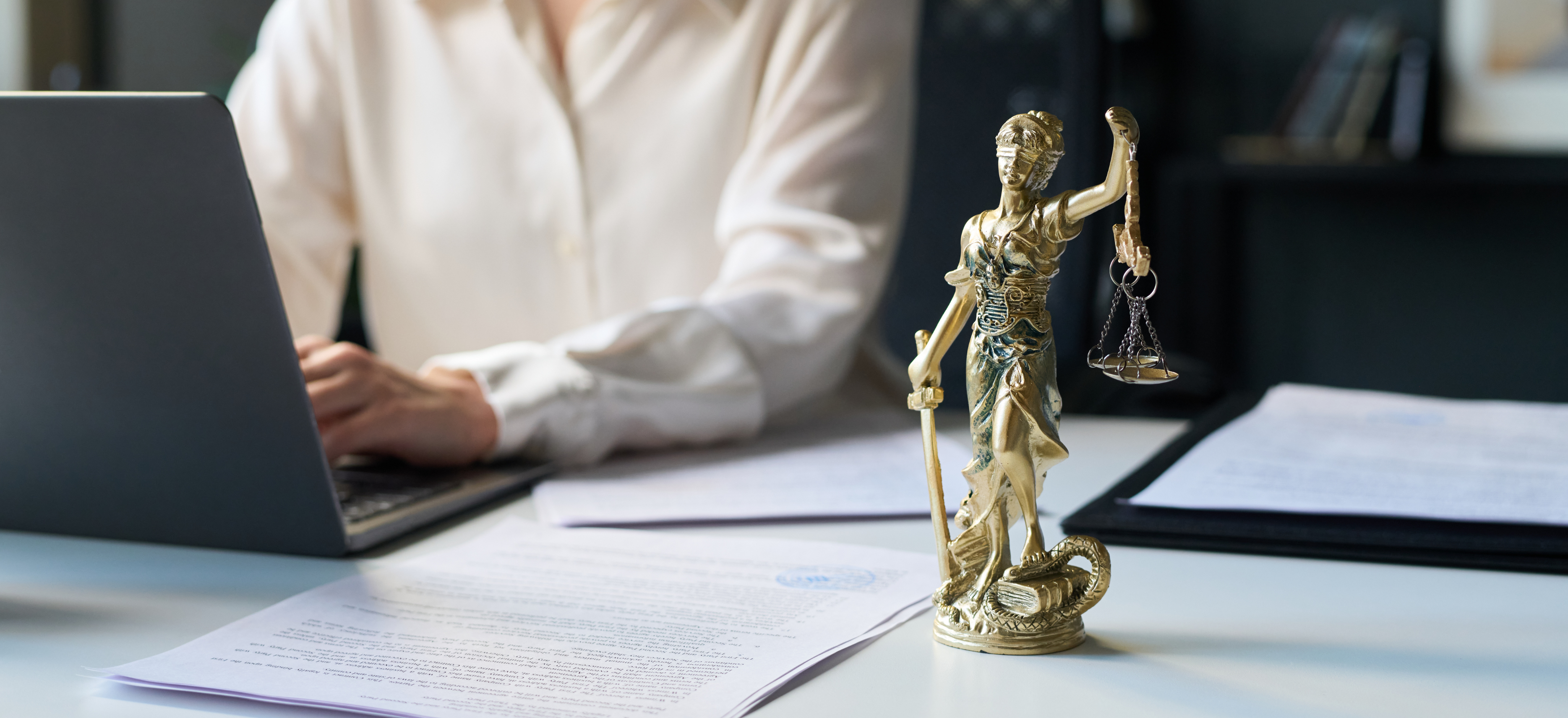 Law firm professional working on a laptop with legal documents and Lady Justice statue