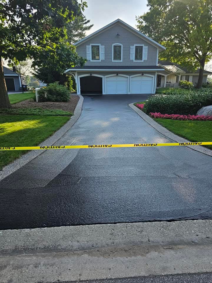 Professional sealcoating equipment and tools on a residential driveway, ready for asphalt maintenance work.
