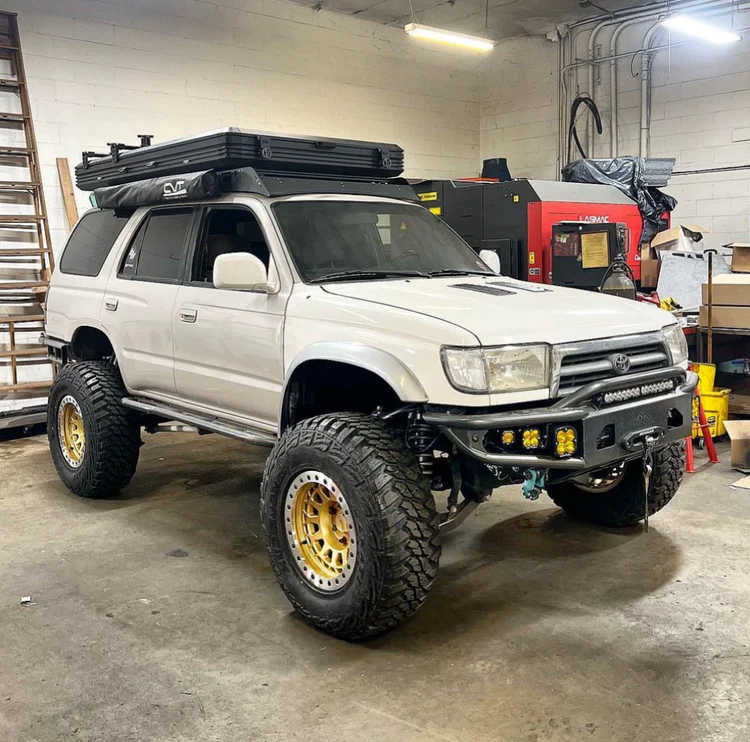 A white off-road SUV with large tires and a roof tent, parked inside a garage workshop.
