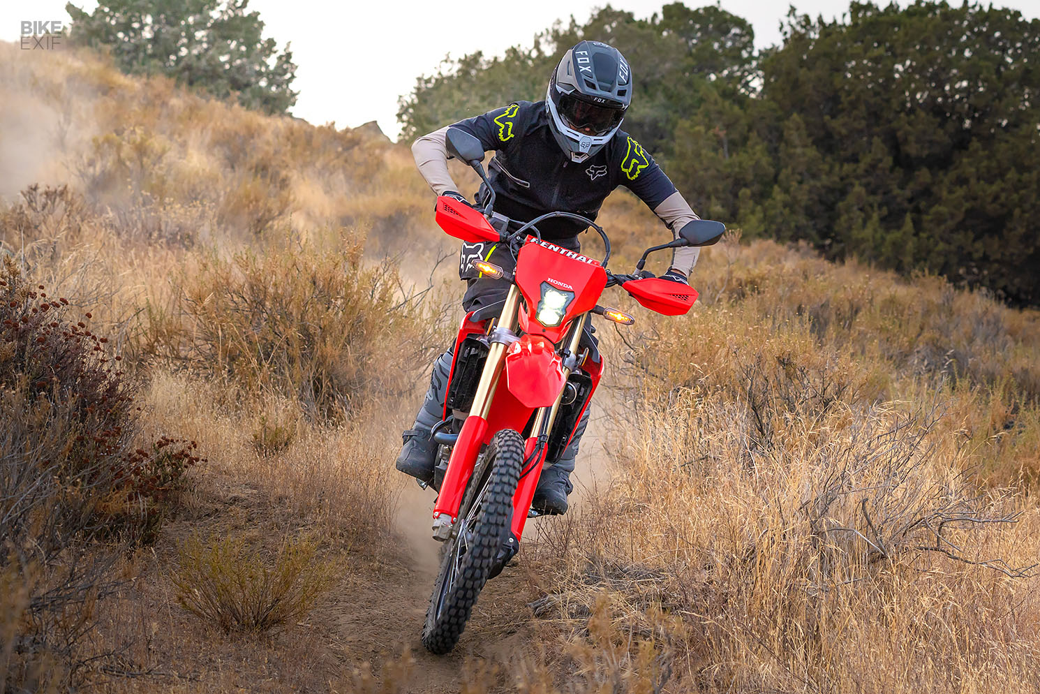 A rider in a black and green motocross gear riding a red motorcycle uphill on a dusty trail. 