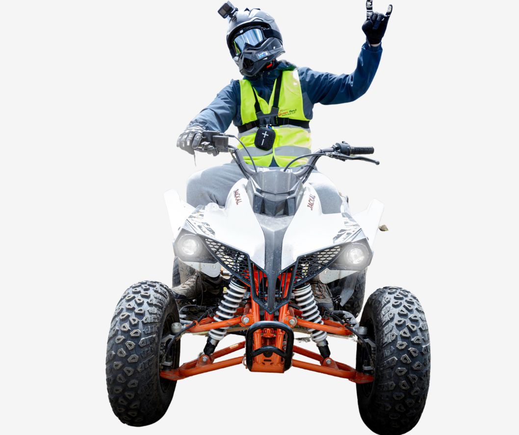A person wearing a black helmet and a yellow safety vest rides an all-terrain vehicle (ATV) with four large tires.