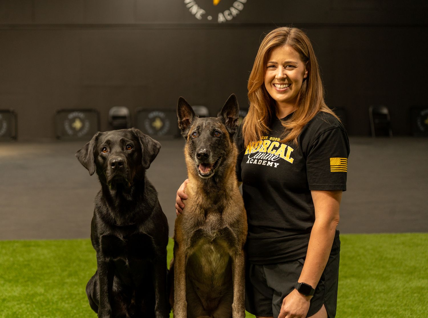 Sam Lee on the training floor with a black labrador and a malinois sitting beside her