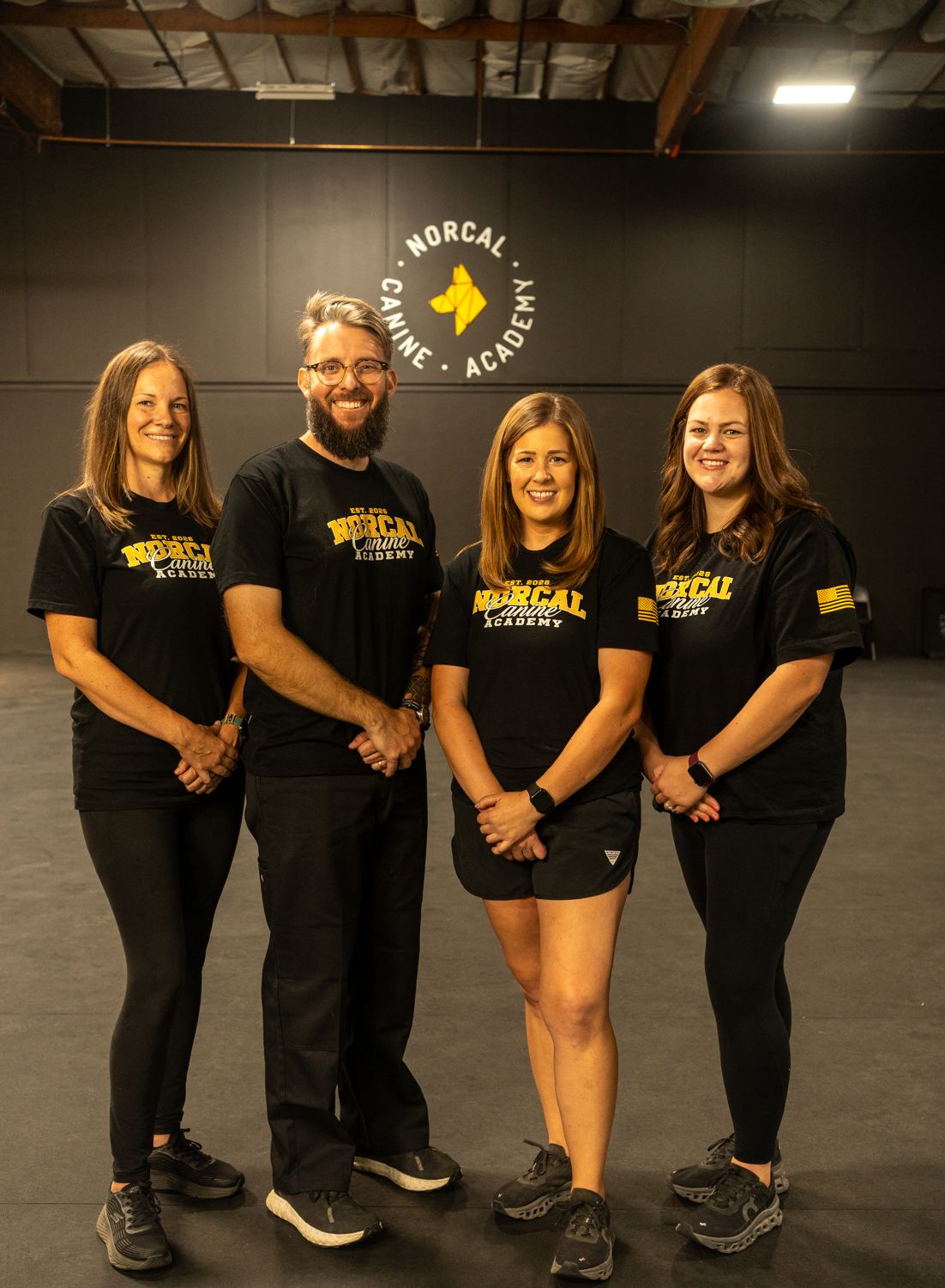 The NorCal Canine Academy team in the training hall, under the academy roundel on the wall