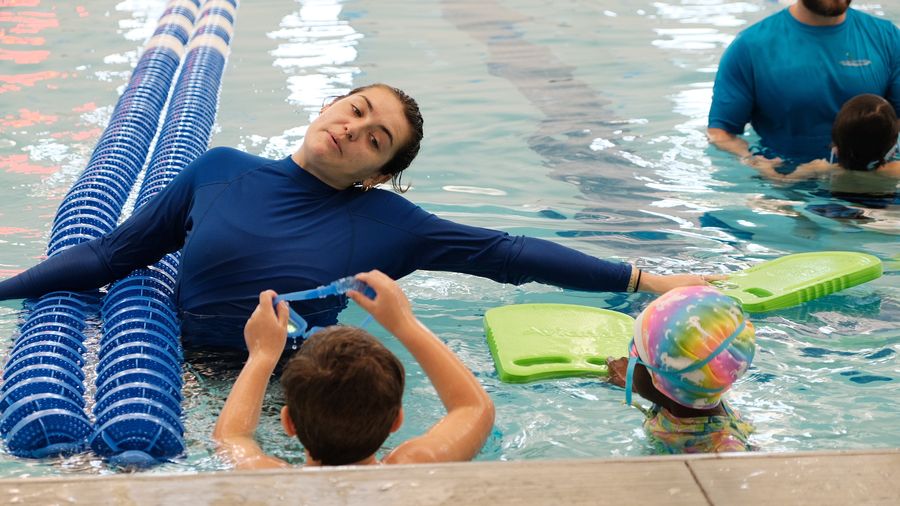 Instructor floating on the lane lines while children watch from the pool wall
